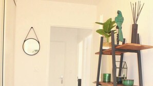 A hallway with a wooden floor, a black stool, a mirror, and a metal ladder shelf with various items. - The SkyFall: superb apartment, terrace and parking space (Longwy)