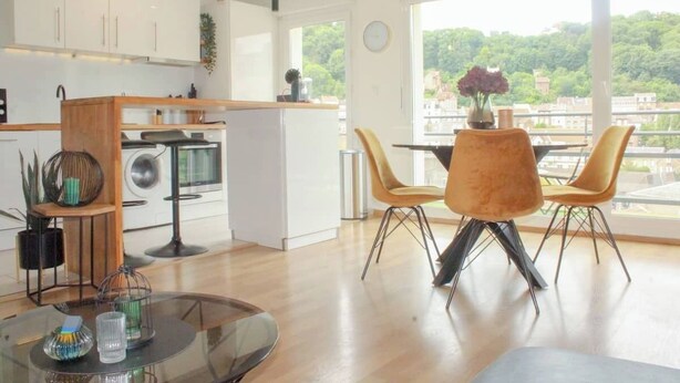 A modern kitchen with white cabinets, a wooden countertop, and a dining area with a glass table and two chairs. - The SkyFall: superb apartment, terrace and parking space (Longwy)