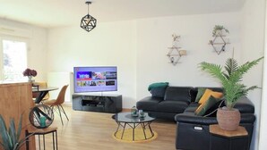 A modern living room with a sofa, coffee table, and TV. There are plants and decorative items on shelves and tables. - The SkyFall: superb apartment, terrace and parking space (Longwy)