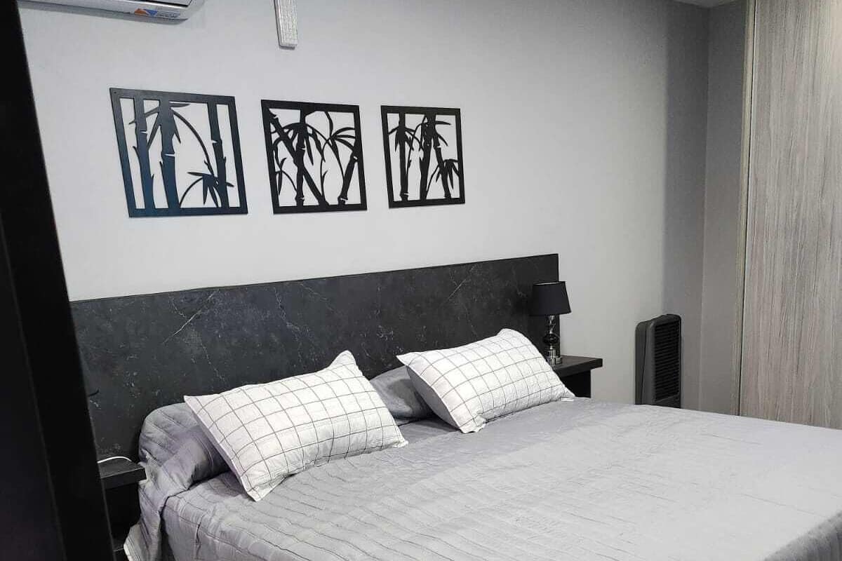 A neatly made bed with a grey quilt and pillows, a black headboard, and three wall-mounted artworks depicting bamboo.