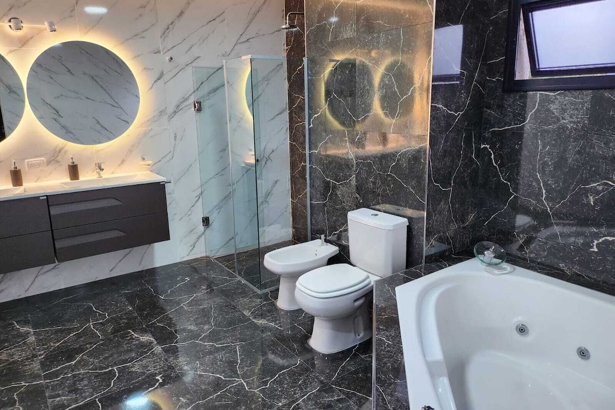 A modern bathroom with a marble vanity, a toilet, a bathtub, and a glass shower enclosure.