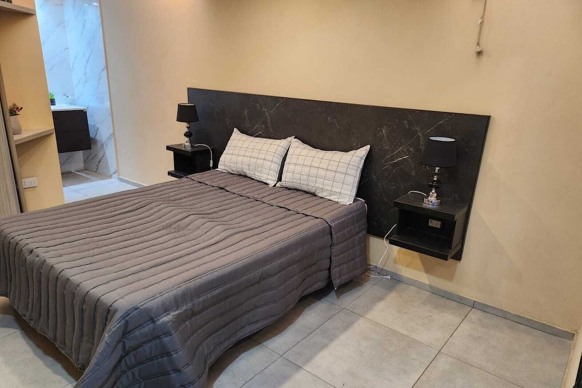 A bedroom with a large bed, two bedside tables, a TV, and a marble wall.