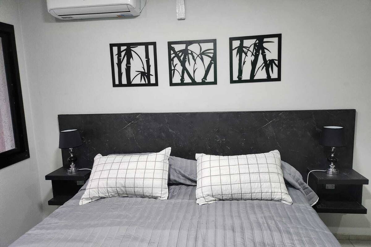 A bedroom with a bed, two bedside tables, a headboard, and three wall-mounted artwork pieces.