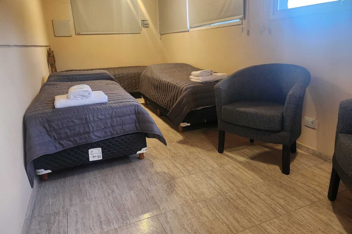 A hotel room with two beds, a chair, and a window.