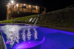 En swimmingpool med en fontän, solstolar och en byggnad i bakgrunden.
