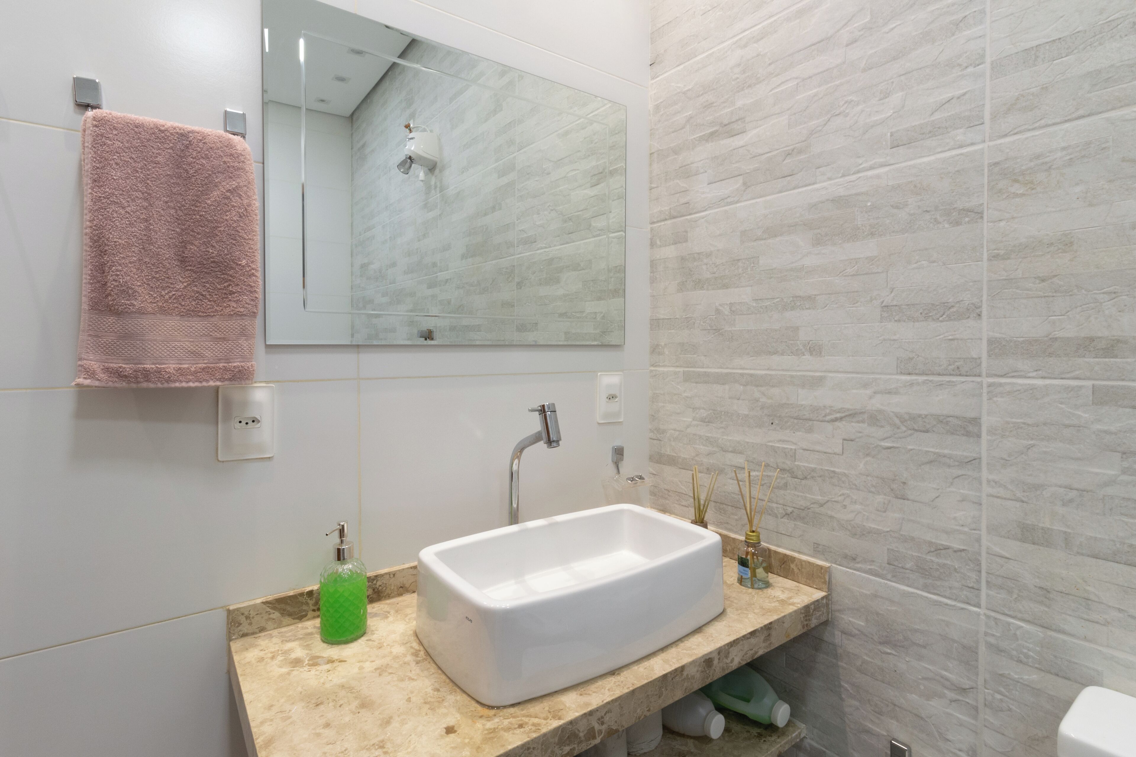 Une salle de bain avec un lavabo blanc, un miroir, une serviette rose et un distributeur de savon vert.