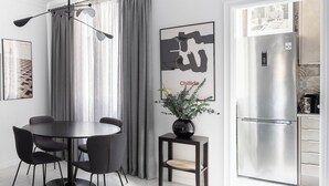 A modern kitchen with a stainless steel refrigerator, a dining area with a round table and chairs, and a wall with a framed artwork.