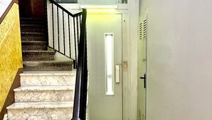 A marble staircase with a black balustrade leading to a door with a light switch and a vent.