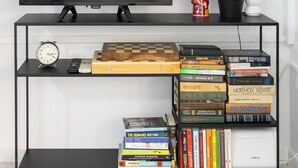 A flat-screen TV on a black TV stand, a cactus plant, a figurine, and a bookshelf with books and a clock.