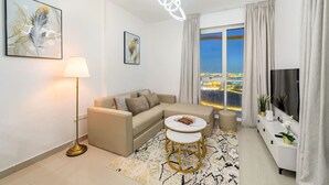 A modern living room with a sofa, a coffee table, a lamp, and artwork on the walls. - Stylish 1BR Retreat in Dubai | Lake Views, Pool, Gym & Prime City Location (Dubai Production City)