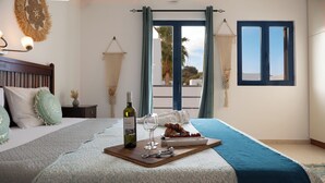 Un lit bien fait, avec un plateau contenant de la nourriture, du vin et une bouteille. Une fenêtre avec des rideaux offre une vue sur des palmiers.