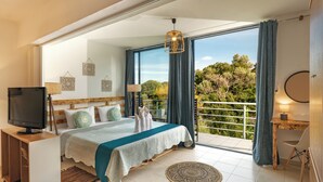 Une chambre à coucher comprenant un lit, une télévision, un bureau et un balcon avec vue sur les arbres.