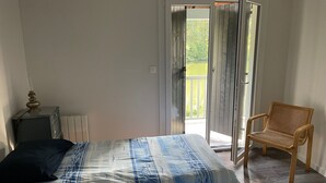 A bedroom with a bed, a chair, a small table, and a sliding glass door leading to a balcony. - L'Eau Posée - Standing gîte facing the Yonne river (Villecien)