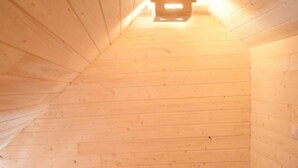 Ein kleiner Raum mit Holzwänden und schrägem Dach, ausgestattet mit einem Einzelbett.