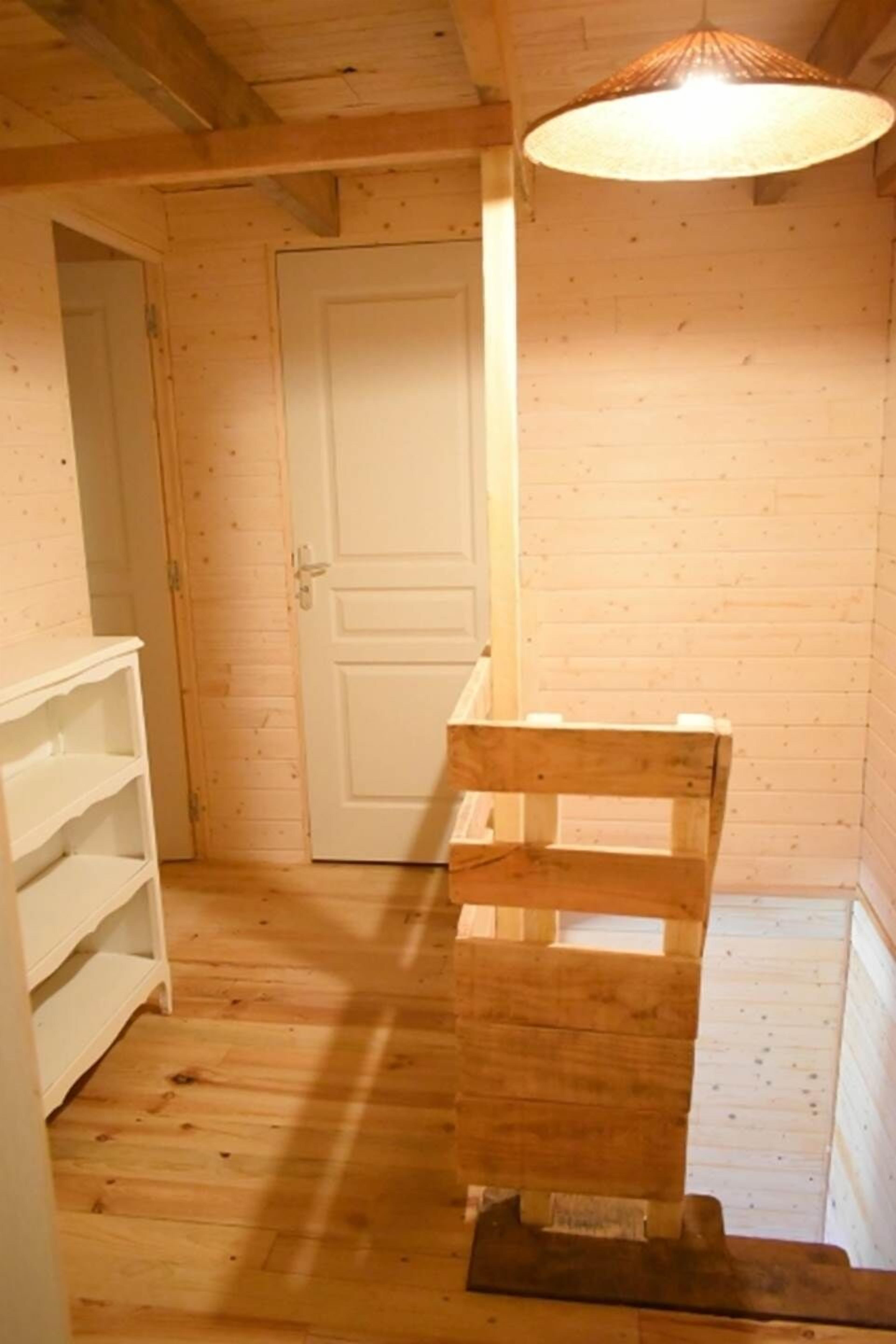 A wooden interior with a white door, a wooden bench, and a white shelving unit.
