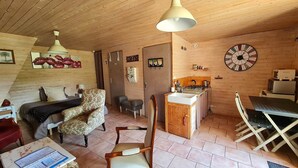 Ein gemütliches Blockhäuschen im Inneren mit Holzbalkendecke, einem Essbereich mit Tisch und Stühlen, einer Küche mit Herd und Spüle sowie einer großen Wanduhr.