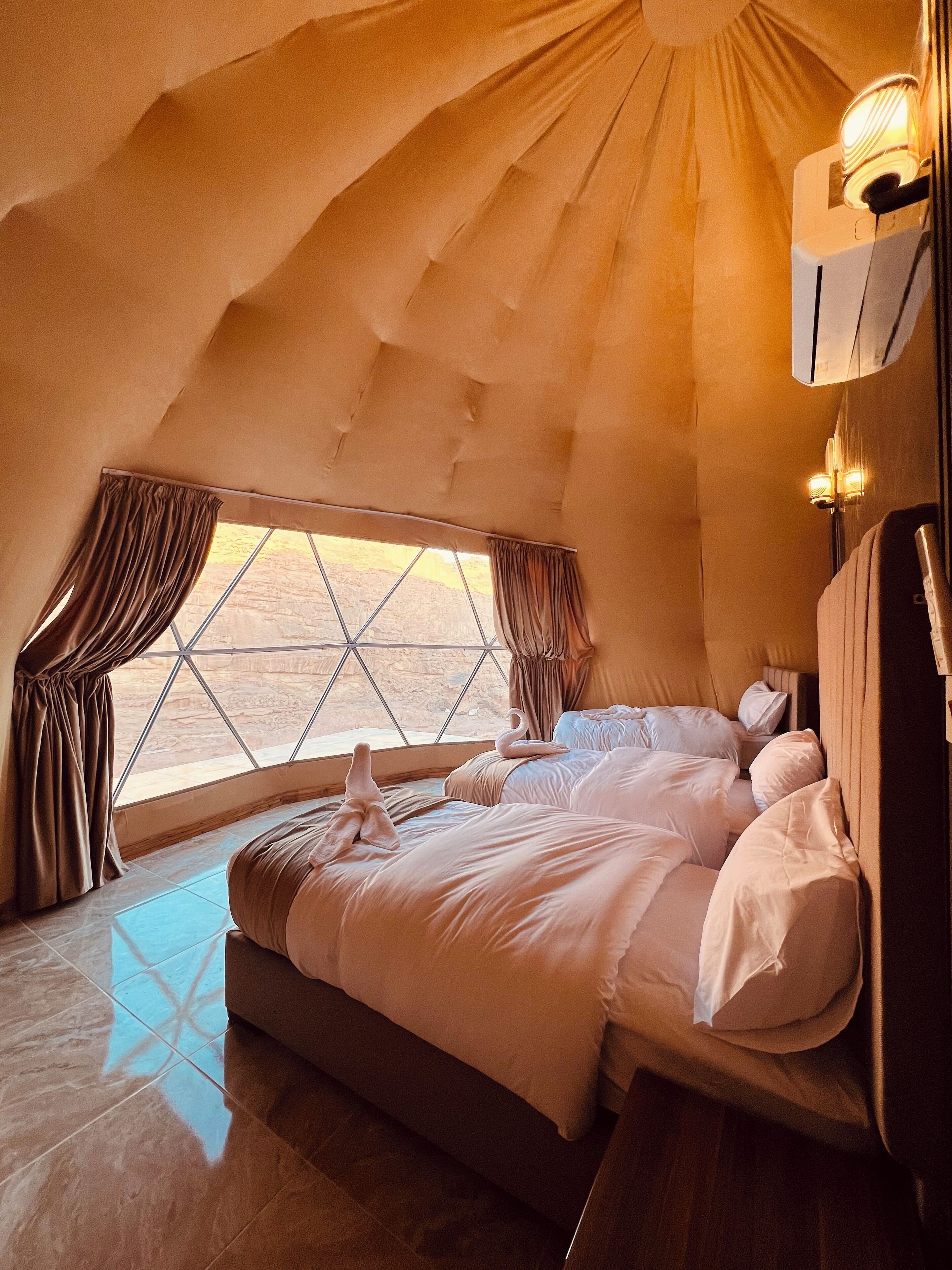 A spacious room with a large bed, a window with curtains, and a unique tent-like ceiling structure.