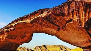 Una formación rocosa arqueada natural con un paisaje desértico al fondo.