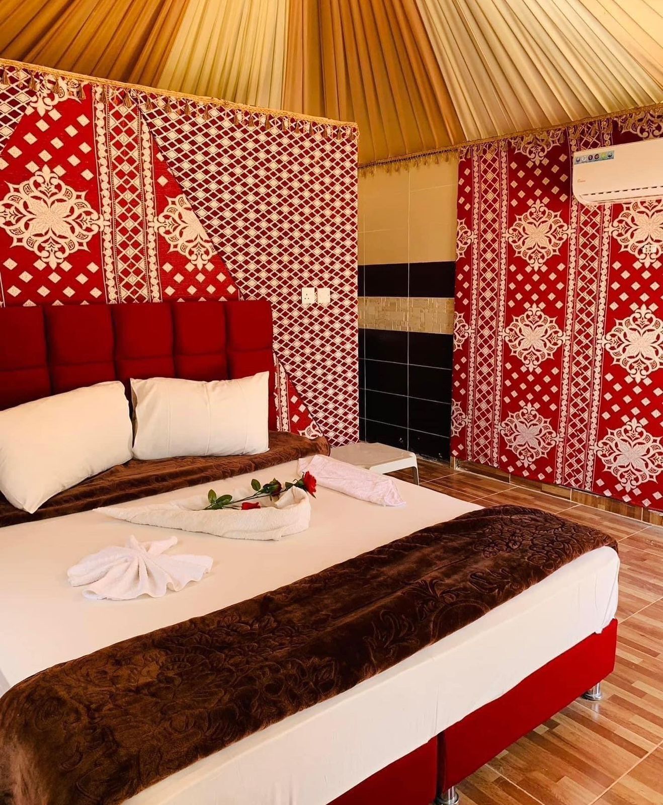 Un dormitorio amplio con una cama grande, paredes con un estampado rojo y blanco, y techo de madera.