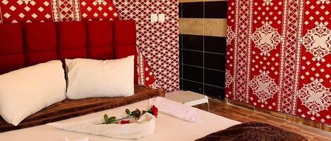 A spacious bedroom with a large bed, red and white patterned walls, and a wooden ceiling.