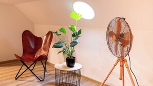 A room with a wooden floor, a red leather chair, a small round table with a potted plant, a standing fan, and a ceiling light fixture. - Soulscape Apartment CityCenter - compact & luxurious loft apartment in the city center (Zwickau)