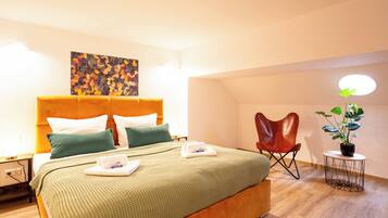 A hotel room with a bed, a headboard, a painting, a chair, a table with a plant, and a lamp.