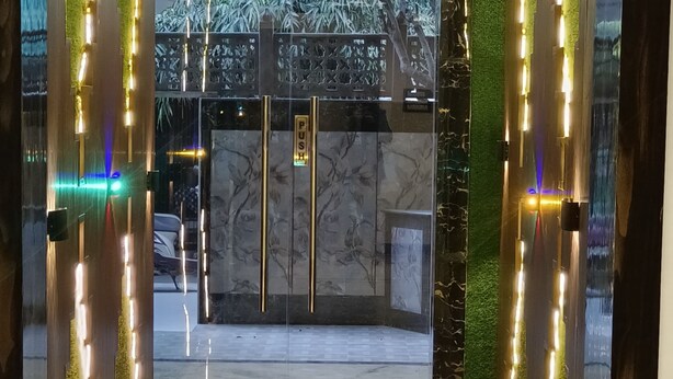 A hotel entrance with a glass door, illuminated by vertical lights, and a sign indicating the direction to the parking area. - Hotel Devvanshi Vila (Varanasi)