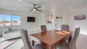A modern dining area with a wooden table and four chairs, a ceiling fan, recessed lighting, a flat-screen TV, and a view of the outside. - Ocean views, steps to beach, family, dining, shops (San Diego)