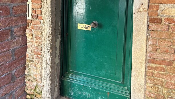 A green door with a sign that reads "PLEASE CLOSE THE DOOR" and a number "2652" above it.