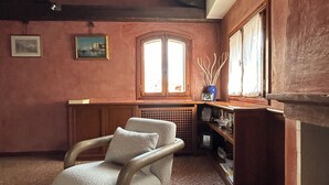 A cozy room with a wooden chair, a patterned rug, a fireplace, and a window with curtains.
