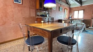 A dining area with a wooden table and clear chairs, a blue pendant light, and a kitchen in the background.
