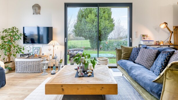 A modern living room with a large TV, a sofa, a coffee table, and a view of a garden through a sliding door. - Amazing home in Venon with WiFi (Venon)