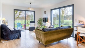 A spacious living room with a large sofa, a coffee table, and a TV. There are large windows offering a view of the outdoors. - Amazing home in Venon with WiFi (Venon)