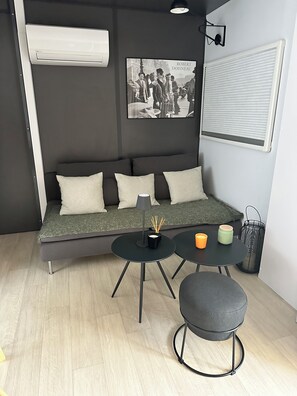 A modern living room with a sofa, two round tables, a lamp, candles, and a framed picture on the wall.
