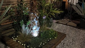 Een goed verlichte tuin met een palmboom, diverse planten en een decoratieve rots.