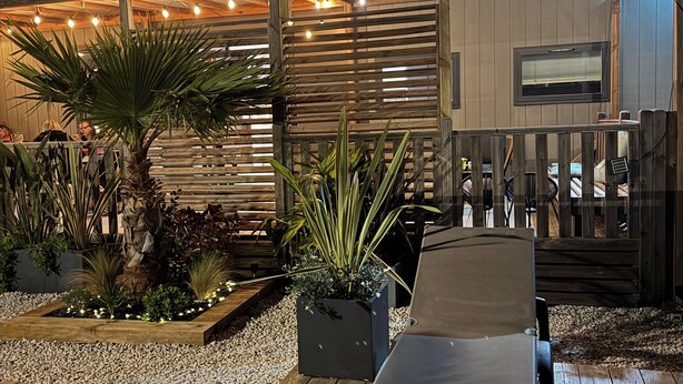 Een terras buiten met een houten bankje, plantenpotten en een houten omheining.