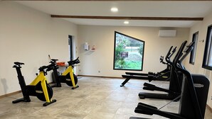 Een sportschool met hometrainers, loopbanden en een groot raam met uitzicht op groen.