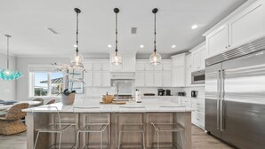 A modern kitchen with white cabinets, stainless steel appliances, and a central island with bar stools. - Pier Park Paradise! Gulf Retreat, Private Pool, Sleeps 24 (Panama City Beach)