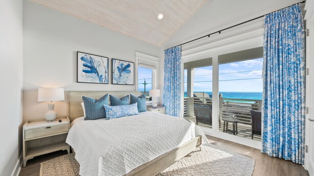 A bedroom with a large bed, a nightstand, a lamp, and a view of the ocean through a sliding door. - Pier Park Paradise! Gulf Retreat, Private Pool, Sleeps 24 (Panama City Beach)