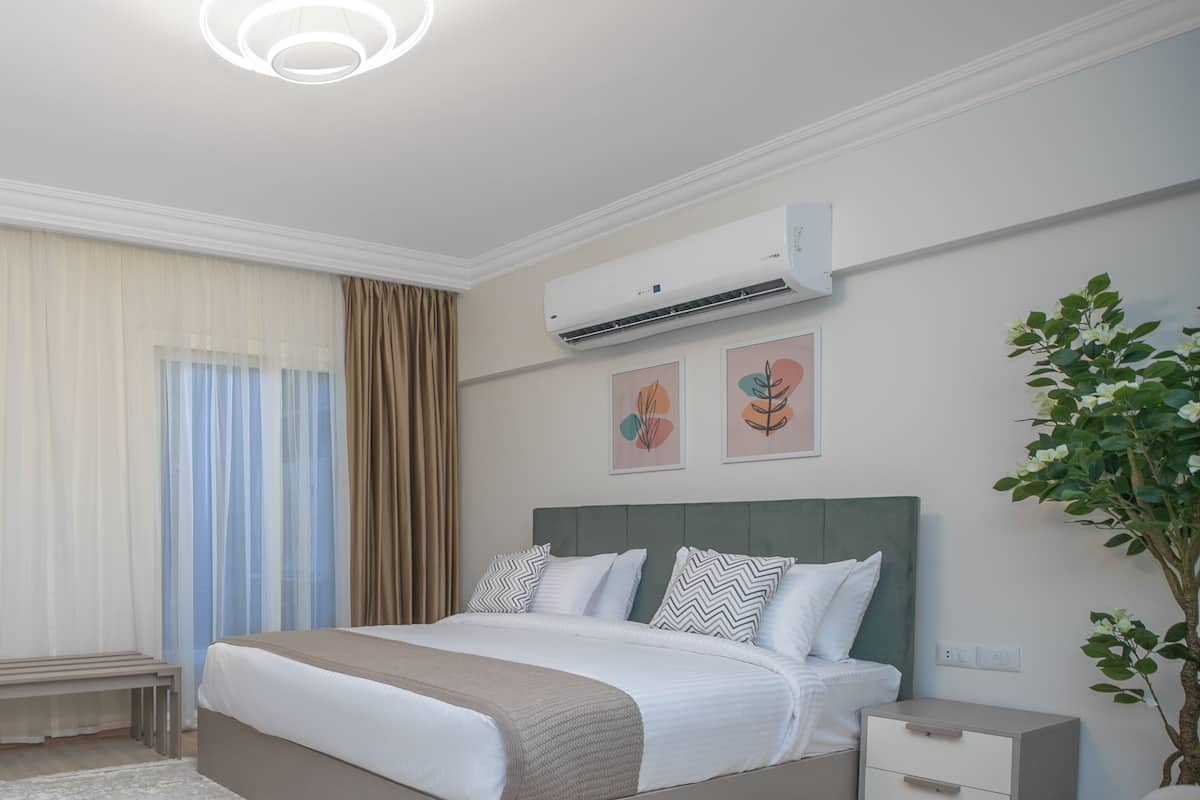 A modern bedroom with a bed, bedside tables, an air conditioner, and a potted plant.