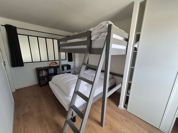 A bunk bed room with a ladder, a bookshelf, and a door.