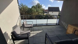 A balcony with two lounge chairs and a small table, offering a view of trees and buildings.