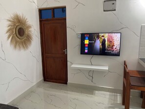 Una habitación con puerta de madera, un televisor de pared mostrando una película y un espejo decorativo con diseño de sol.