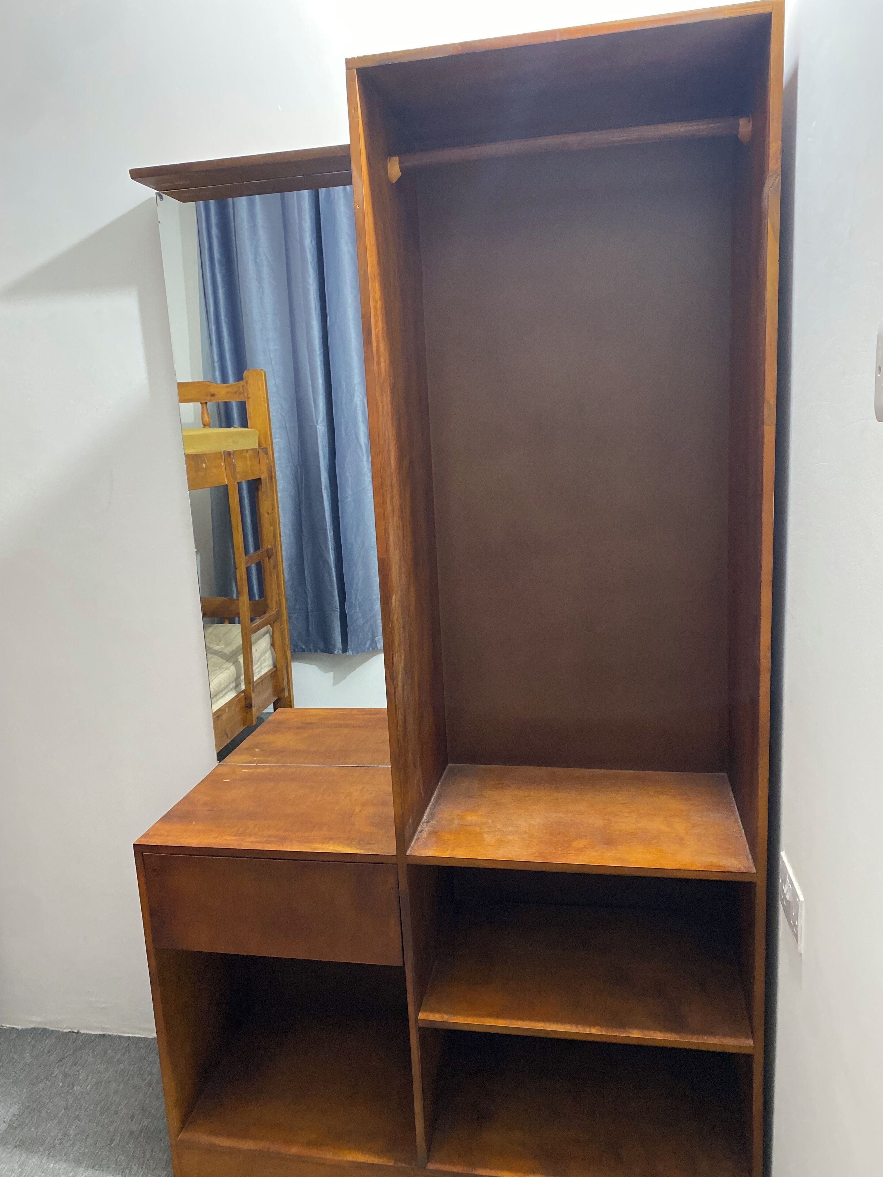 A room with a wooden wardrobe, a wooden chair, and a blue curtain.