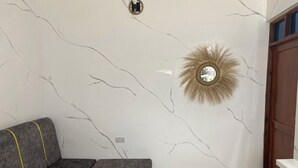 Una habitación con un sofá gris, un tapete redondo, un espejo decorativo y una puerta de madera.