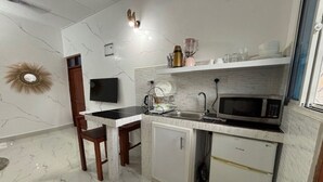 Cocina compacta con piso de mármol, horno microondas integrado, refrigerador pequeño y una silla de madera.