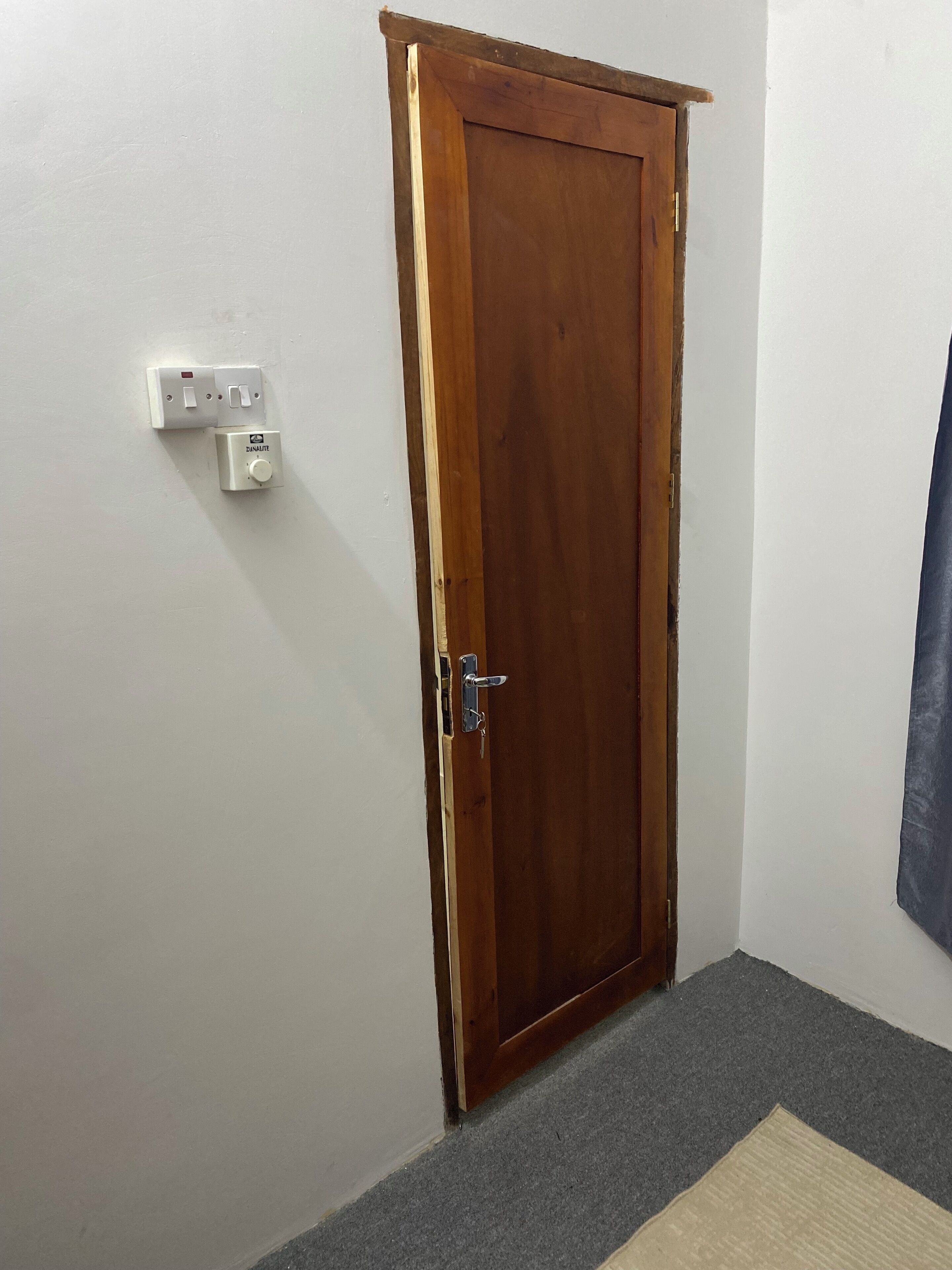 Uma porta de madeira com maçaneta e olho de fechadura, um interruptor de luz e uma tomada na parede.