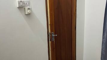 Uma porta de madeira com maçaneta e olho de fechadura, um interruptor de luz e uma tomada na parede.