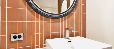 Un baño con lavamanos blanco, un espejo redondo y una pared con azulejos.