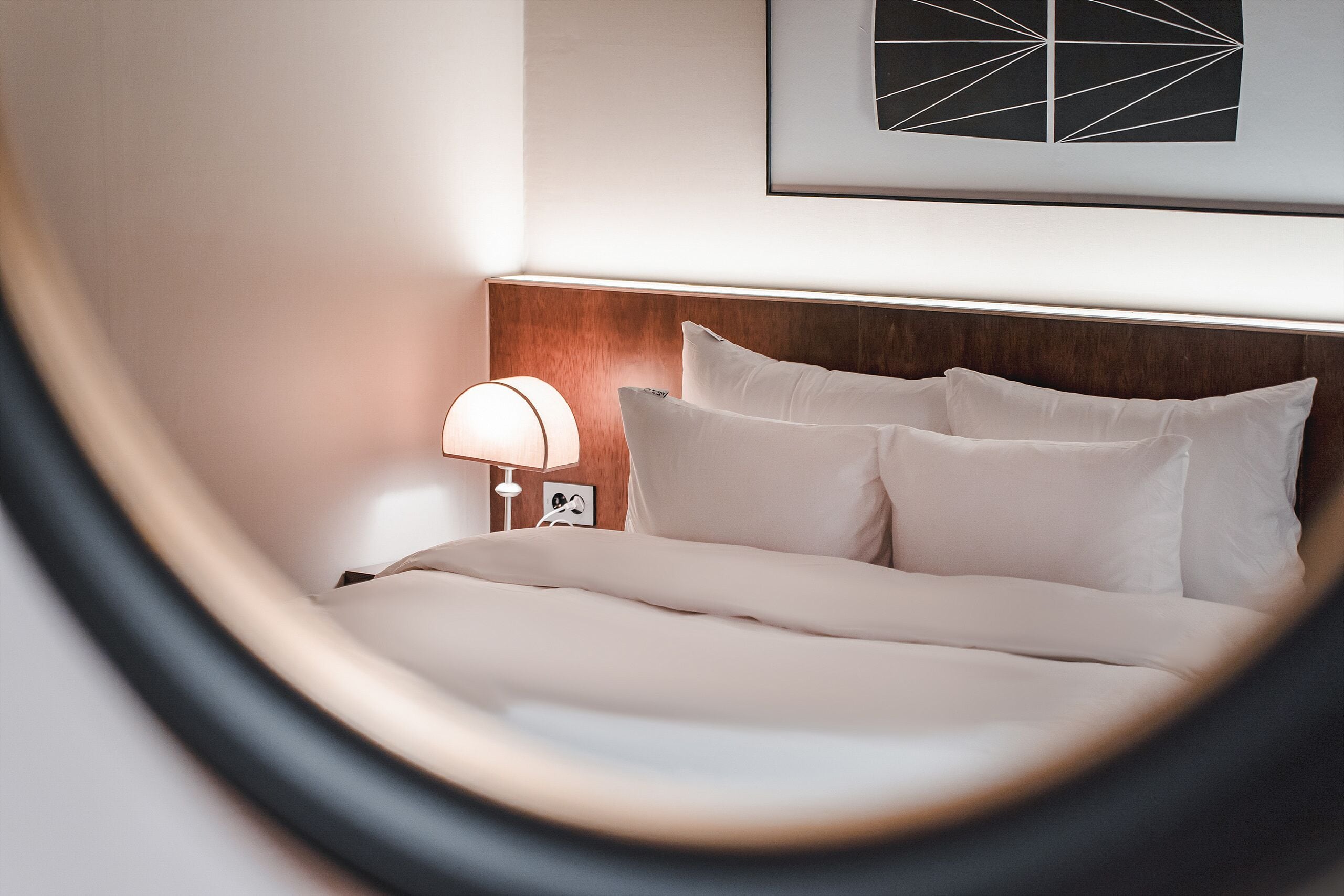 A neatly made bed with white linens, a wooden headboard, and a bedside lamp.